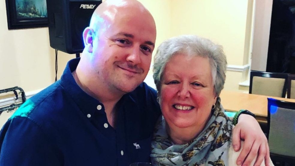 A bald man smiling at the camera with his arm around an older woman, also smiling