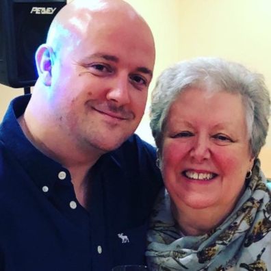 A bald man smiling at the camera with his arm around an older woman, also smiling